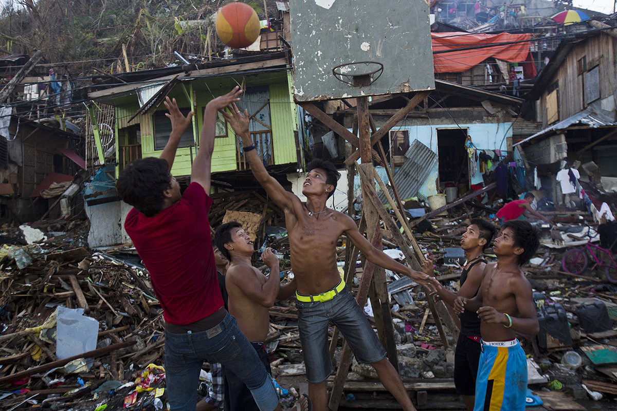 In this Sunday, Nov. 17, 2013 photo, Typhoon Haiyan survivors play basketball in a destroyed neighborhood in Tacloban, Philippines. They found the hoop in the ruins of their obliterated neighborhood. They propped up the backboard with broken wood beams and rusty nails scavenged from vast mounds of storm-blasted homes. A crowd gathered around. And on one of the few stretches of road here that wasn't overflowing with debris, they played basketball. (AP Photo/David Guttenfelder)