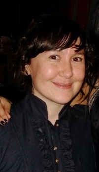A brunette woman in a black shirt smiles at the camera.