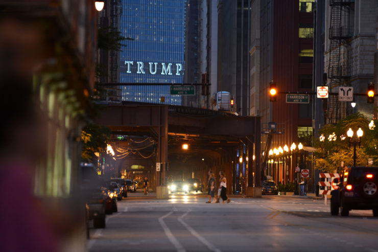 "TRUMP," the letters adorning a skyscraper  standing where the building that long housed the Chicago Sun-Times once stood,  lit up and projecting across the El tracks
