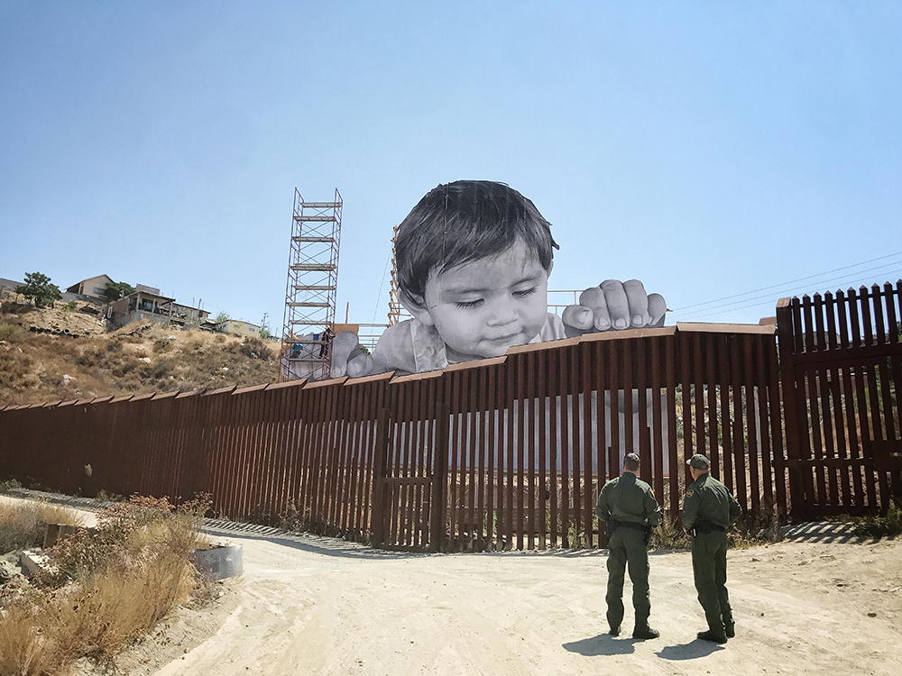 In an installation by the French artist JR, a large photo of a toddler from Tecate, Mexico is visible on the American side of the U.S.-Mexico border wall. When it comes to immigration, the news cycle is often inundated with familiar narratives of Latinx communities or refugees from countries such as Syria