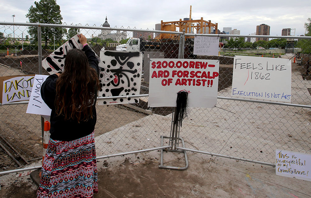 A woman hangs up a protest sign on a construction fence near the controversial sculpture “Scaffold” at the Minneapolis Sculpture Garden in May 2017. The Walker Art Center, which operates the park, ultimately removed the two-story sculpture, by artist Sam Durant, because of protests from Native Americans who say it brought back painful memories of the mass hanging of 38 Dakota men in 1862