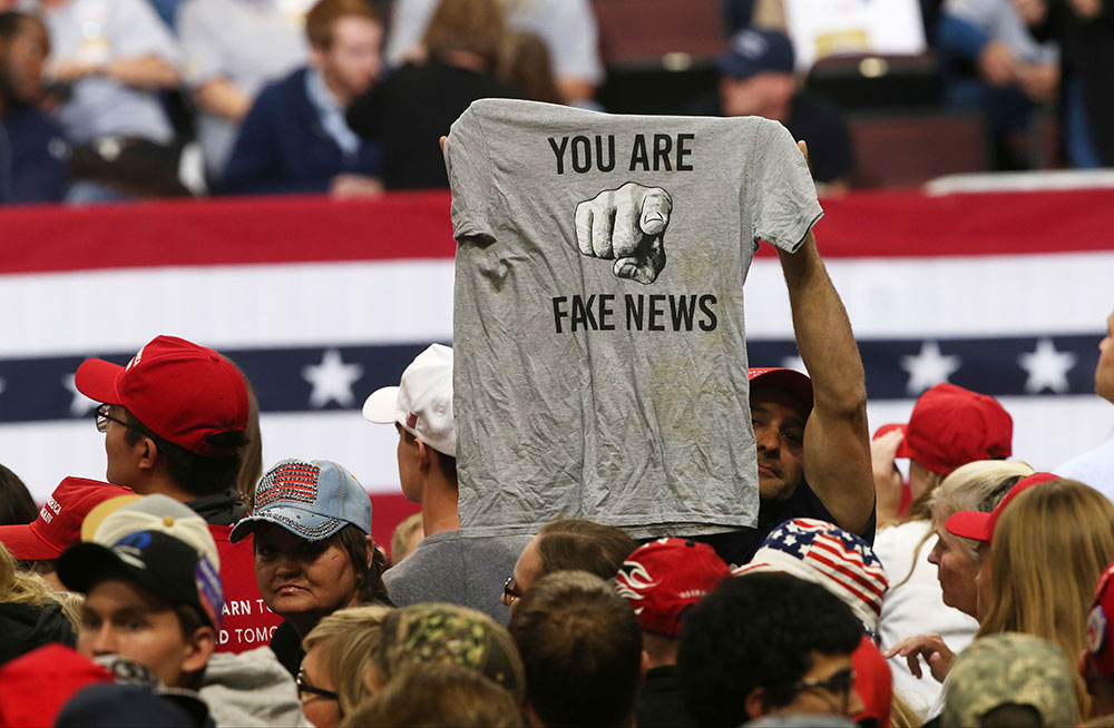 A man holds up a T-shirt ridiculing the news media before a Trump rally in Rochester, Minnesota in October 2018