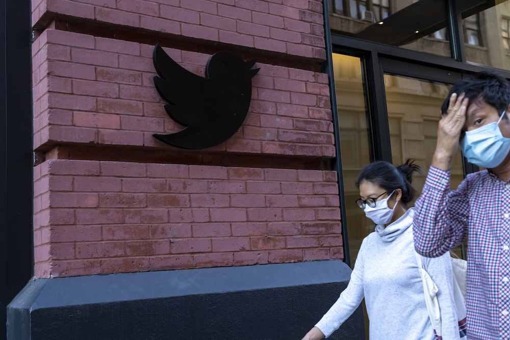 People wearing face masks walk past a Twitter logo outside New York City headquarters