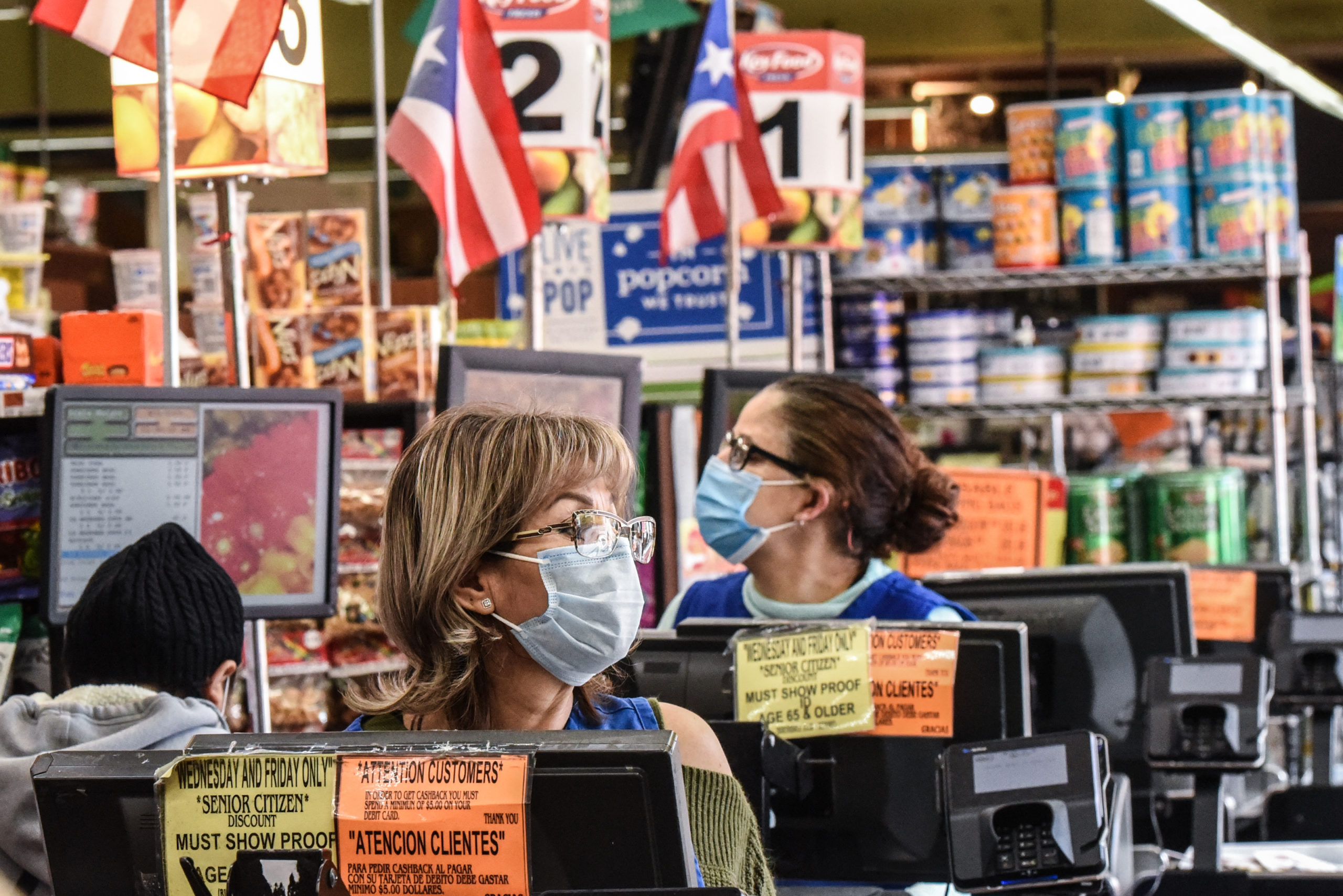 Cashiers wearing protective masks work in a grocery store in the Bushwick neighborhood of Brooklyn in April 2020