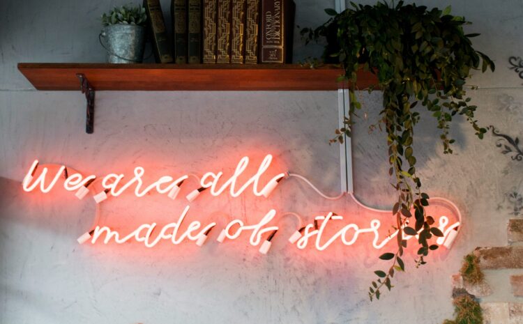 Neon script on a white plaster wall that says "We are all made of stories"